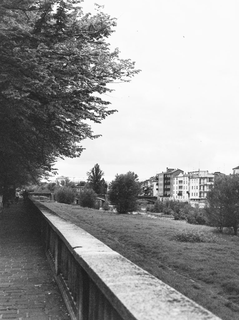 Black and white photograph of a view of the river in Parma from the path alongside it. ©Sarah Beeusaert