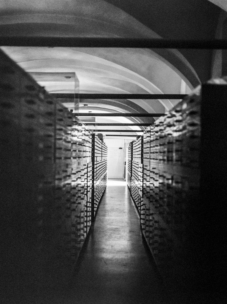 Black and white photograph of the CSAC archives, a long corridor of metal drawers. ©Sarah Beeusaert